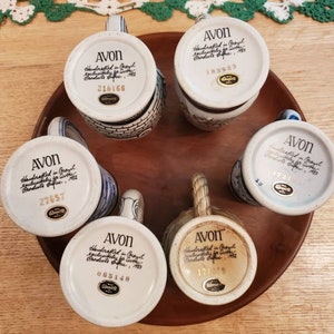 Pode incluir: Seis canecas de cer&acirc;mica branca com detalhes azuis e dourados. Cada caneca tem um design diferente e apresenta um r&oacute;tulo manuscrito na parte inferior que diz "AVON Handcrafted in Germany exclusively for Avon Products Office, 1983" e um n&uacute;mero &uacute;nico.
