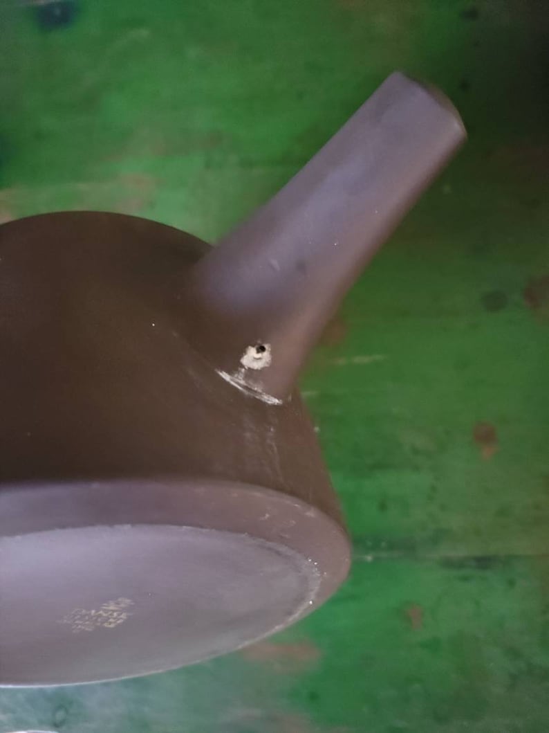 Op de afbeelding: Een donkergrijze theepot van keramiek met een tuit en een klein gaatje aan de zijkant. De theepot staat op een groene ondergrond.