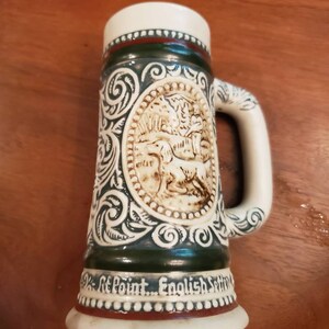 Pode incluir: Uma caneca de cerveja de cer&acirc;mica com um design verde e branco. A caneca apresenta uma imagem em relevo de um c&atilde;o em uma cena de floresta. A parte inferior da caneca diz "St. Point... English Setter".
