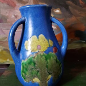 May include: A blue ceramic vase with two handles and a floral design. The vase has a crackled glaze and features yellow, green, and red accents.