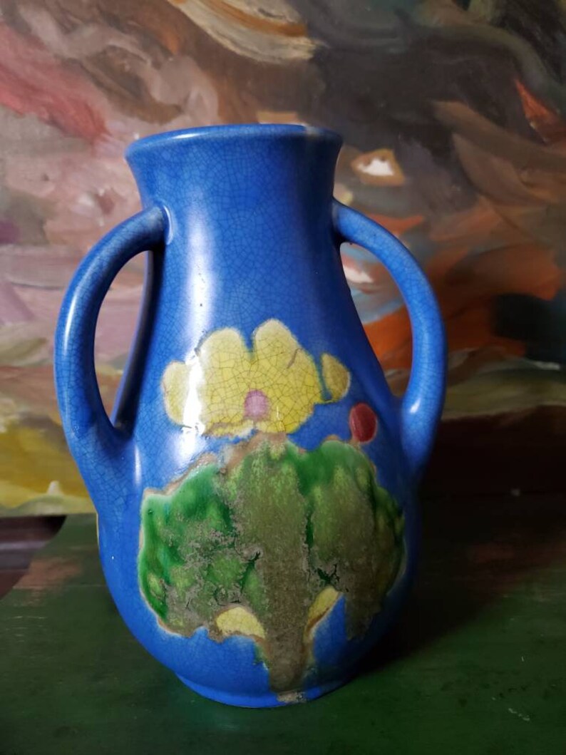 May include: A blue ceramic vase with two handles and a floral design. The vase has a crackled glaze and features yellow, green, and red accents.