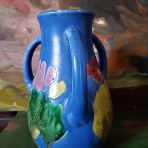 May include: A blue ceramic vase with two handles and a crackled glaze. The vase is decorated with colorful flowers and leaves.