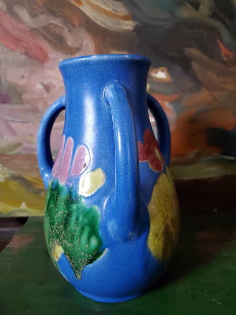 May include: A blue ceramic vase with two handles and a crackled glaze. The vase is decorated with colorful flowers and leaves.