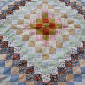May include: A patchwork quilt with a central diamond pattern in shades of pink, green, and brown. The quilt is made of various fabrics with floral and geometric designs.