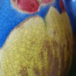 May include: Close-up of a ceramic object with a cracked glaze. The glaze is yellow with a blue and red design. The cracks in the glaze are visible and create a textured surface.