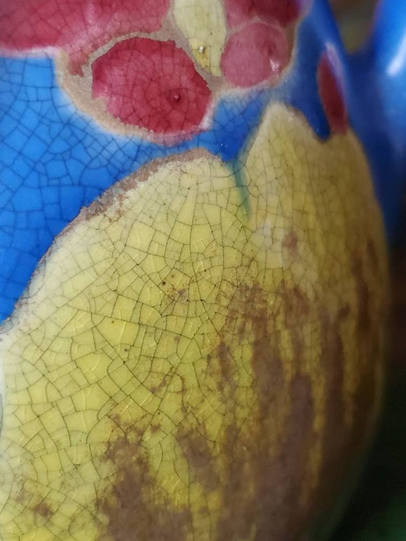 May include: Close-up of a ceramic object with a cracked glaze. The glaze is yellow with a blue and red design. The cracks in the glaze are visible and create a textured surface.
