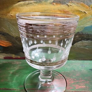 May include: A clear glass goblet with a gold and white etched design. The goblet has a round base and a stem.