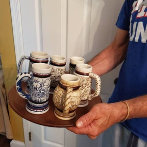 Pode incluir: Um conjunto de seis canecas de cerveja de cer&acirc;mica com designs intrincados, com um esquema de cores azul e branco. As canecas s&atilde;o exibidas em uma bandeja de madeira.