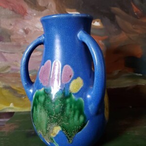 May include: A blue ceramic vase with two handles and a floral design in shades of pink, green, and yellow.