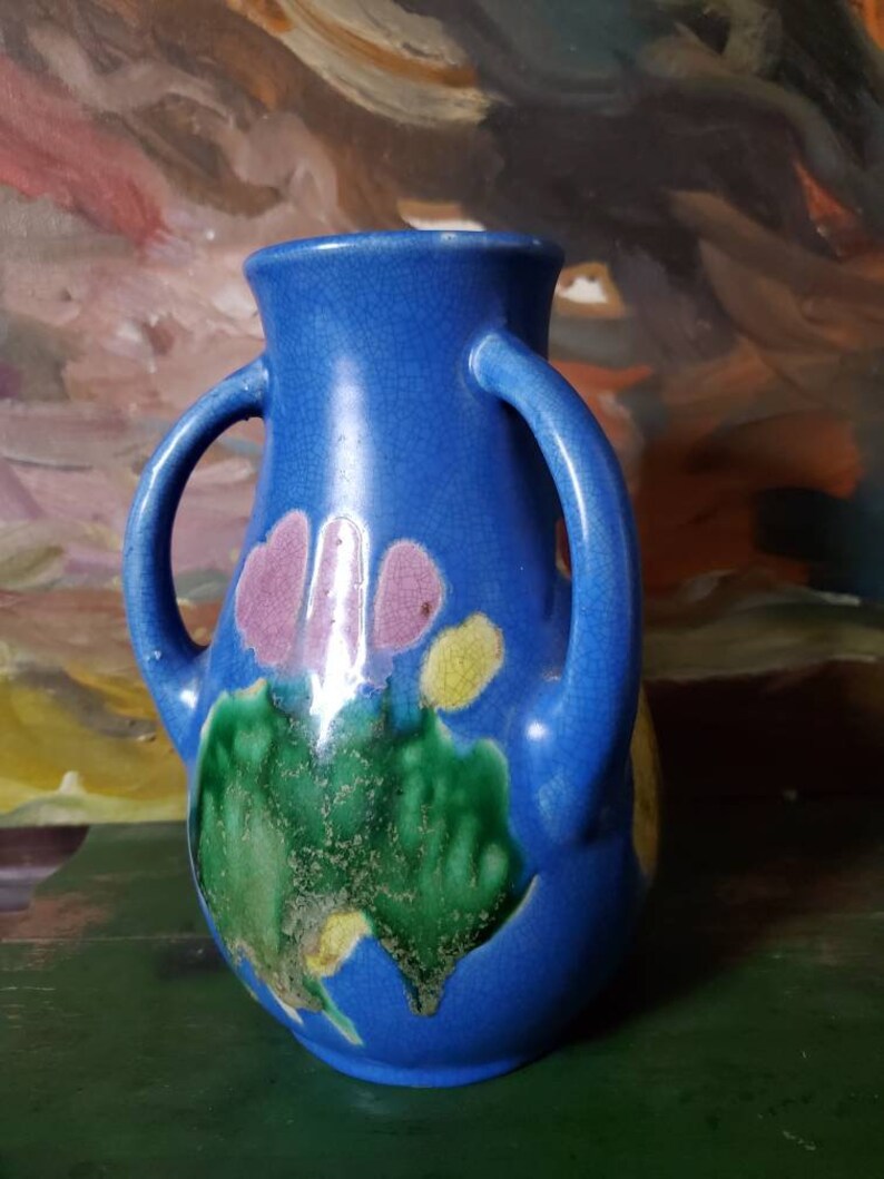 May include: A blue ceramic vase with two handles and a floral design in shades of pink, green, and yellow.