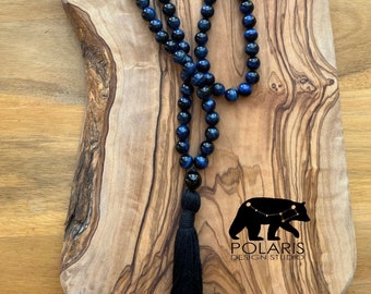 May include: A blue and black gemstone mala necklace with a black tassel. The necklace is made of 108 beads and is approximately 18 inches long. The beads are round and have a smooth, polished finish. The tassel is made of black thread and is approximately 3 inches long.