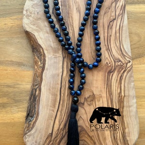 May include: A blue and black gemstone mala necklace with a black tassel. The necklace is made of 108 beads and is approximately 18 inches long. The beads are round and have a smooth, polished finish. The tassel is made of black thread and is approximately 3 inches long.