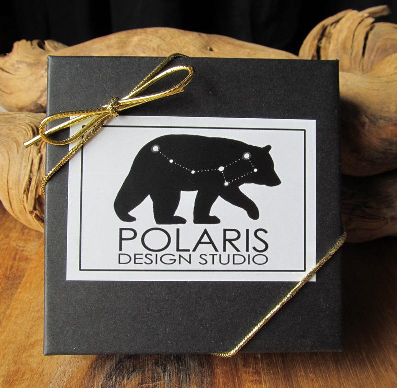 May include: A black gift box with a white label featuring a black bear constellation design and the text "POLARIS DESIGN STUDIO." The box is tied with a gold ribbon.