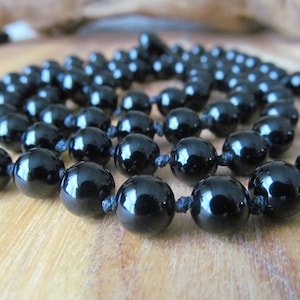 May include: A black beaded necklace with a knotted cord. The beads are round and glossy.