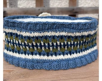 May include: A blue knit headband with a geometric pattern in white, navy, and olive green. The headband has a ribbed texture and a soft, white interior. The item is designed to keep the ears and forehead warm.