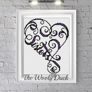 May include: A purple and white cross-stitch pattern of a heart with swirls. The pattern is framed and the text "The Wooly Duck" is at the bottom of the frame.