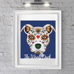 May include: A white dog face with a Day of the Dead sugar skull design. The dog's face is decorated with colourful flowers, hearts, and swirls. The background is a solid blue.