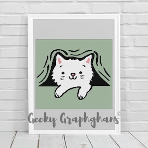 May include: A framed print featuring a white cat peeking out from under a green blanket. The cat has pink ears and a smiling face. The print is in a white frame and has the text "Geeky Graphghans" at the bottom.