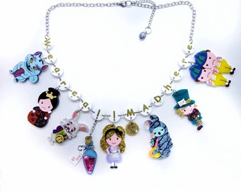 Può includere: Una collana bianca con lettere dorate che compongono la frase "We're all mad here" e ciondoli con personaggi di Alice nel Paese delle Meraviglie, tra cui il Cappellaio Matto, la Regina di Cuori, il Gatto del Cheshire e il Coniglio Bianco.