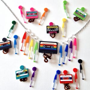May include: A silver chain necklace with a rainbow cassette tape charm and rainbow colored dangle charms. The necklace also features several pairs of cassette tape earrings with different colored designs.