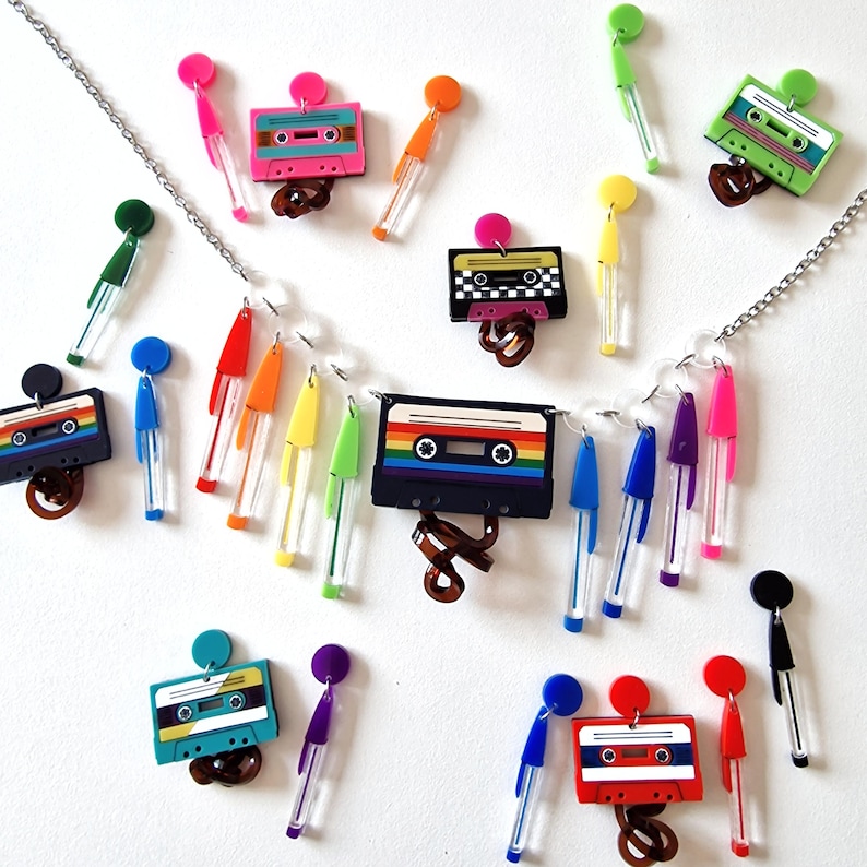 May include: A silver chain necklace with a rainbow cassette tape charm and rainbow colored dangle charms. The necklace also features several pairs of cassette tape earrings with different colored designs.