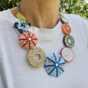 May include: A colorful necklace with fruit and floral designs. The necklace features a variety of shapes, including circles, stars, and flowers. The colors are bright and vibrant, including red, orange, yellow, green, blue, and white.