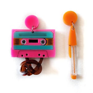 May include: A pair of earrings featuring a pink cassette tape with a turquoise and orange design and a bright orange stick-like earring.