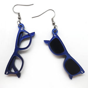 Può includere: Un paio di orecchini a forma di occhiali da sole blu. Gli orecchini sono in metallo e hanno un ciondolo in acrilico blu a forma di occhiali da sole.