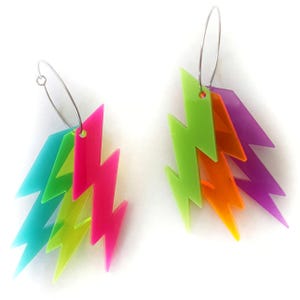 Op de afbeelding: Een paar kleurrijke oorbellen met een bliksemontwerp. Elke oorbel heeft meerdere lagen neonkleurige acryl bliksemschichten in roze, groen, blauw, oranje en paars, opgehangen aan zilveren hoepels. Opvallende sieraden.