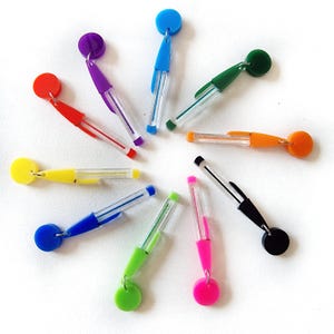 May include: Ten colorful pens with clear barrels and a small round disc at the top. The pens are arranged in a circle on a white background.