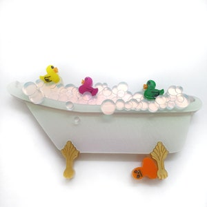 May include: A white porcelain bathtub with gold feet filled with soapy bubbles and three rubber duckies. One duck is yellow, one is pink, and one is green.