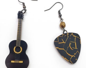 May include: A pair of asymmetrical earrings. One earring is a miniature black guitar with gold accents. The other is a black guitar pick with a gold geometric design and a small gold bead. Both earrings have dark metal hooks.