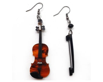 May include: A pair of earrings featuring a brown violin and a black bow. The violin has a black and white string design and a white tuning peg. The bow is black with a silver hook.