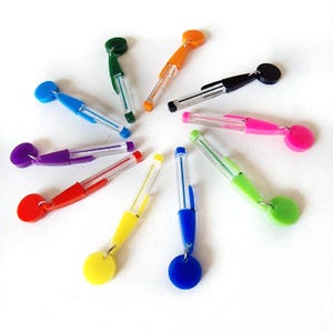 May include: A set of ten colorful retractable pens with clear barrels and round, colored caps. The pens are arranged in a circle on a white background.