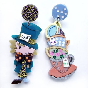 Può includere: Un paio di orecchini fantasiosi con un personaggio del Cappellaio Matto con un cappello blu e una pila di tazze da tè con pois e motivi floreali. L'orecchino del Cappellaio Matto ha un'etichetta 10/6 sul suo cappello.
