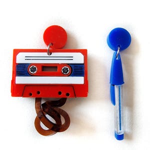 May include: A pair of earrings, one shaped like a red cassette tape with a brown tape spool hanging from it, and the other shaped like a blue pen.