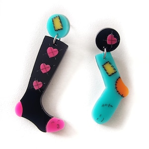 May include: A pair of colourful sock-shaped earrings. One earring is black with pink hearts and the other is turquoise with yellow and orange patches.
