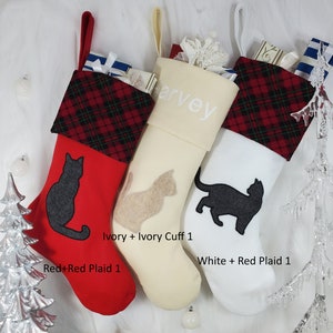 May include: Three Christmas stockings with red and white plaid cuffs. The stockings are personalized with the name "Harvey" and feature a black cat silhouette. The stockings are made of ivory, white, and red fabric.
