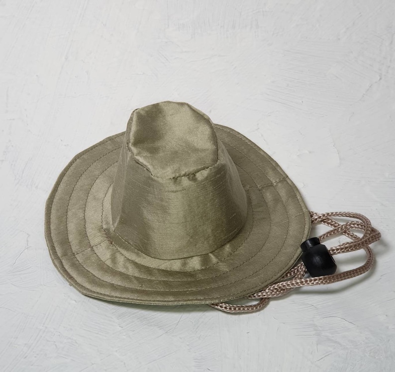 Puede incluir: Un sombrero de sol verde caqui con un ala ancha y un cord&oacute;n.