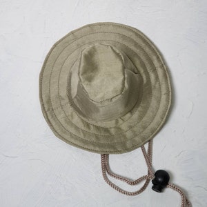 Puede incluir: Un sombrero de sol verde caqui con un ala ancha y un cierre de cord&oacute;n.