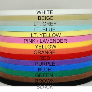 May include: A stack of 14 different colored fabric strips, each with a label indicating its color. The colors are white, beige, light grey, light blue, light yellow, pink/lavender, yellow, orange, red, purple, blue, green, brown, and black.