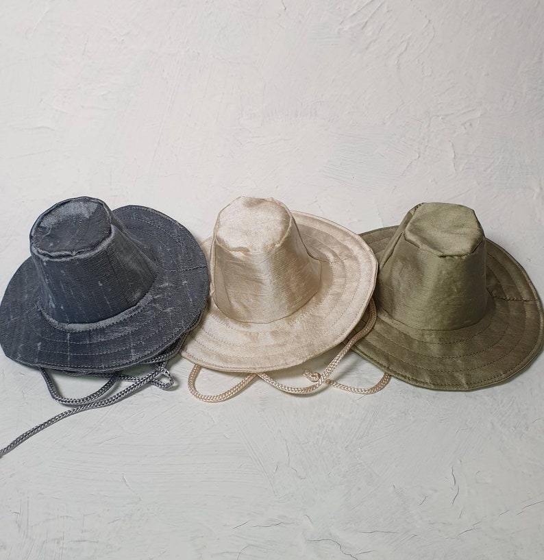 Puede incluir: Tres sombreros de ala ancha de diferentes colores. Los sombreros est&aacute;n hechos de un tejido texturizado y tienen una ala ancha. Los sombreros est&aacute;n dispuestos en fila, con el sombrero gris a la izquierda, el sombrero beige en el centro y el sombrero verde a la derecha.