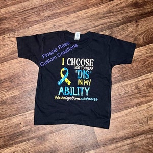 May include: Black t-shirt with a yellow and blue ribbon and the text "I CHOOSE NOT TO WEAR "DIS" IN MY ABILITY #downsyndromeawareness"