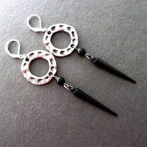 May include: A pair of silver-toned earrings with a textured circular design. Each earring features a black bead and a long, black, pointed pendant. The earrings have a lever-back closure.