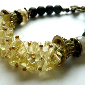 May include: A gold and black bracelet with a cluster of clear yellow faceted beads and a large gold bead with a decorative design.