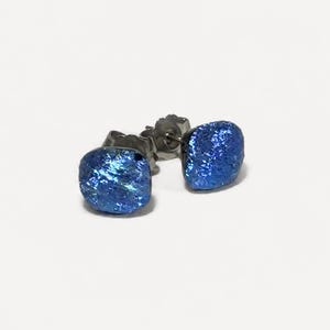 May include: A pair of stud earrings featuring small, square-shaped components with a vibrant, metallic blue textured surface. The earrings have a dark metal post and backing mechanism visible behind the blue square faces, designed for pierced ears.