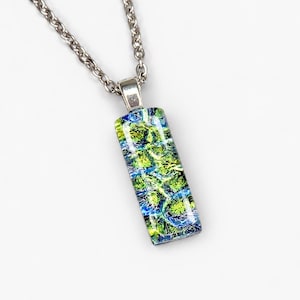 May include: A rectangular glass pendant necklace featuring a vibrant abstract pattern of lime green, deep blue, and black swirls. The pendant is suspended from a silver-toned metal chain, showcasing a polished finish and a smooth, reflective surface.