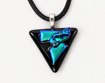 May include: A triangular black glass pendant featuring layered iridescent blue and green dichroic glass accents. The pendant is attached to a silver-toned metal bail and hangs from a black woven cord necklace.