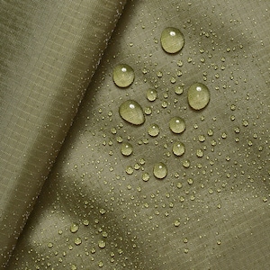 Può includere: Primo piano di un tessuto verde con gocce d'acqua sulla superficie. Il tessuto è liscio e ha una leggera lucentezza. Le gocce d'acqua sono chiare e rotonde, e sono sparse sul tessuto.