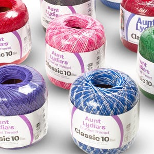 Puede incluir: Múltiples ovillos de hilo de ganchillo Aunt Lydia's Classic 10 en varios colores, incluyendo rojo, rosa, morado, azul y verde. Cada ovillo tiene una etiqueta de papel blanco con detalles morados, mostrando la marca y el texto de tamaño 10.